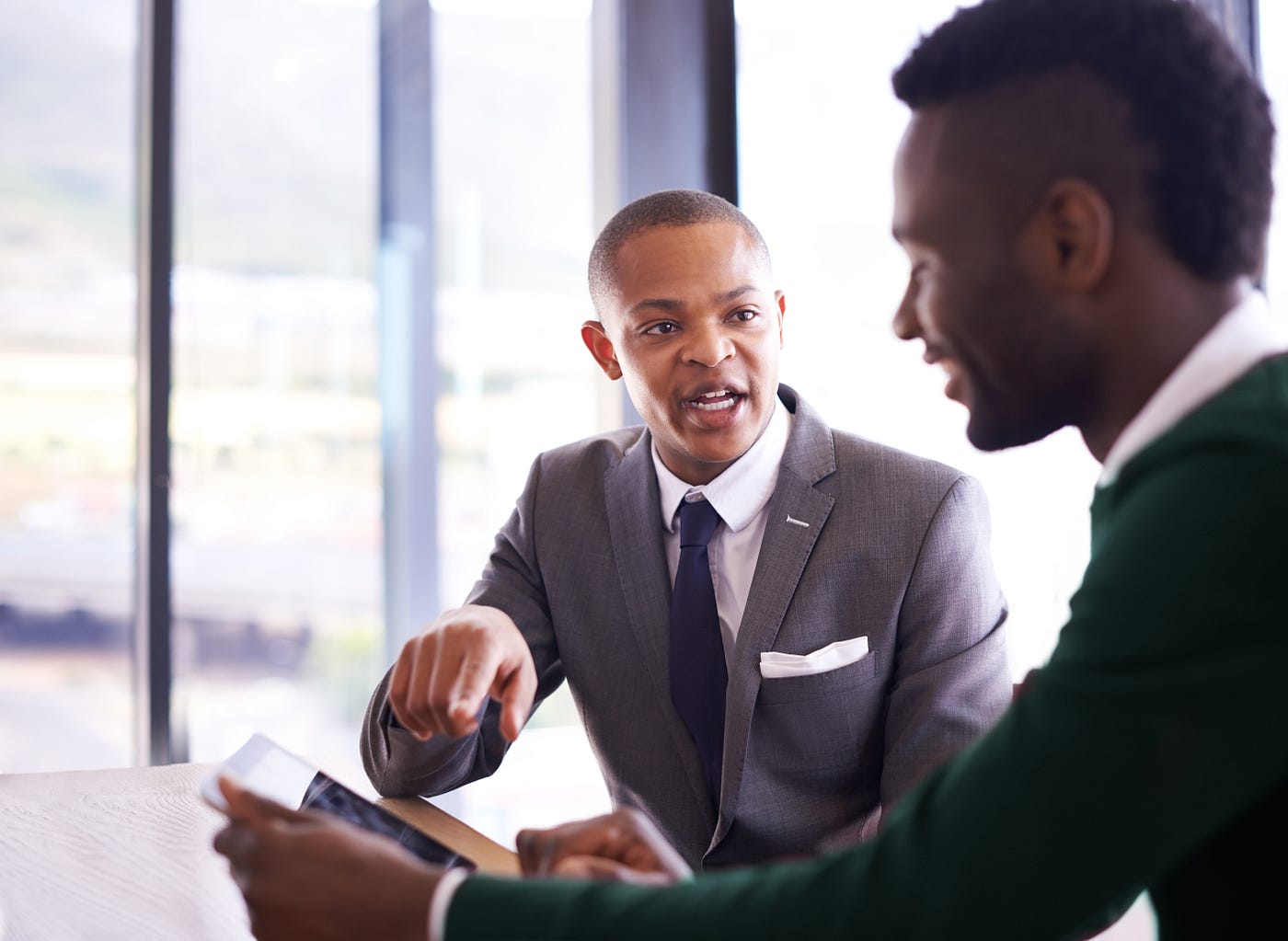 One young businessman gives his colleague some constructive criticism as The colleague looks at his tablet.