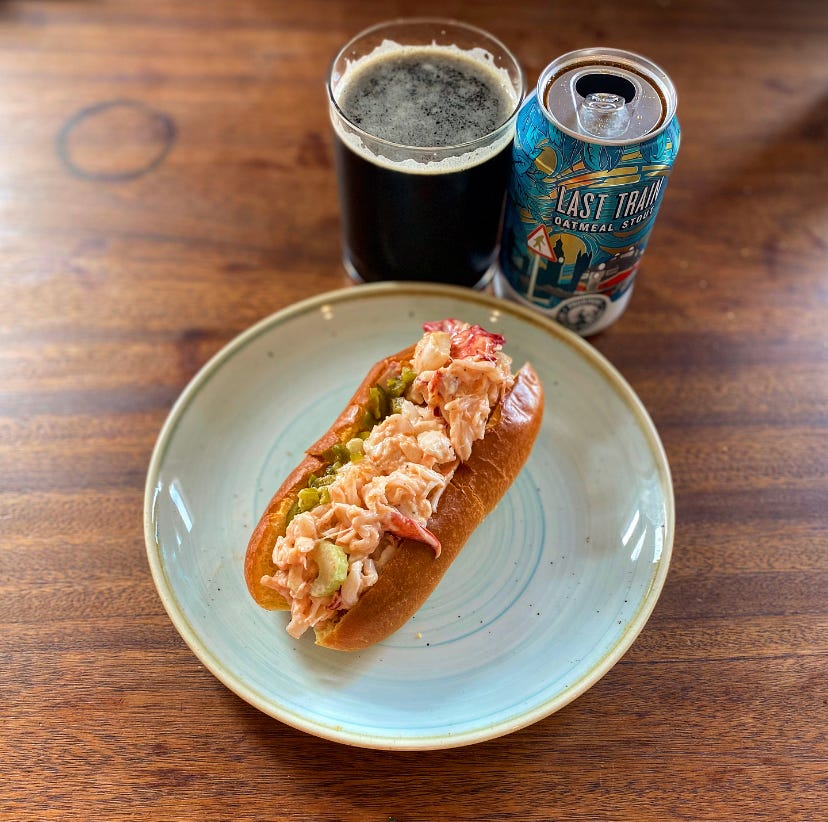Photo of a lobster roll on a plate with a cup of beer next to it.