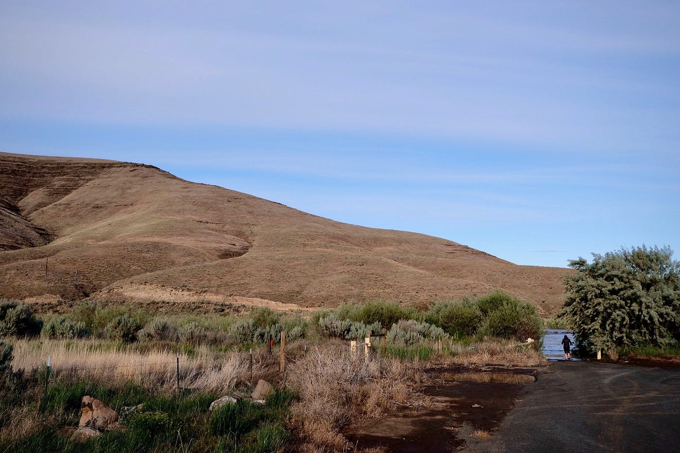 hillside and blue sky, a woman stands the bottom right corner