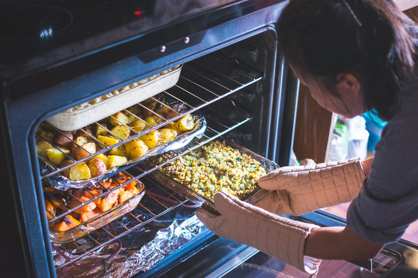 A woman is baking nutritious and delicious vegetables in her oven. Potatoes, carrots and cauliflower. The kitchen smells wonderful.
