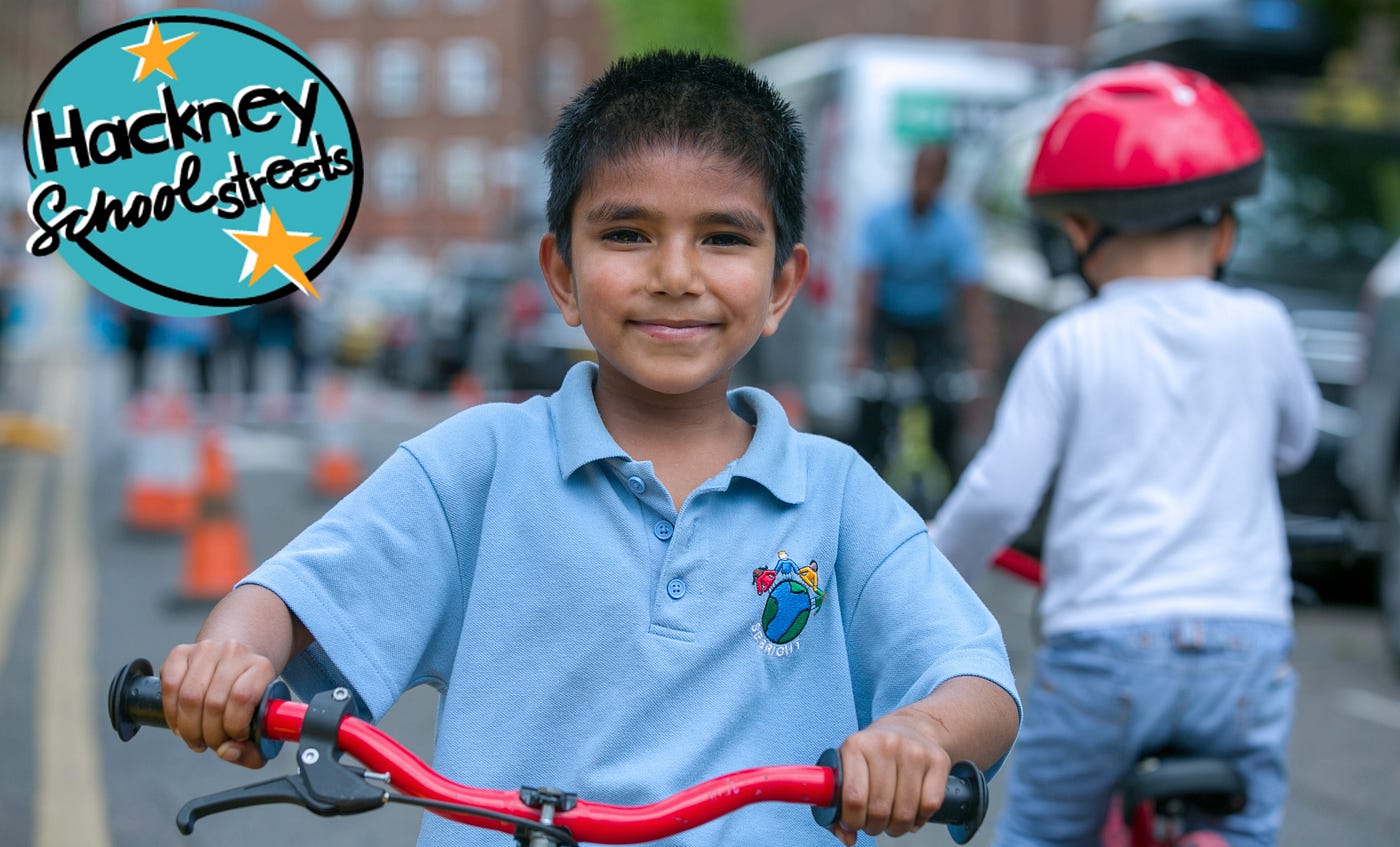 A child on bike smiles into the camera. The aqua-and-yellow “Hackney School Streets” logo is in the corner.