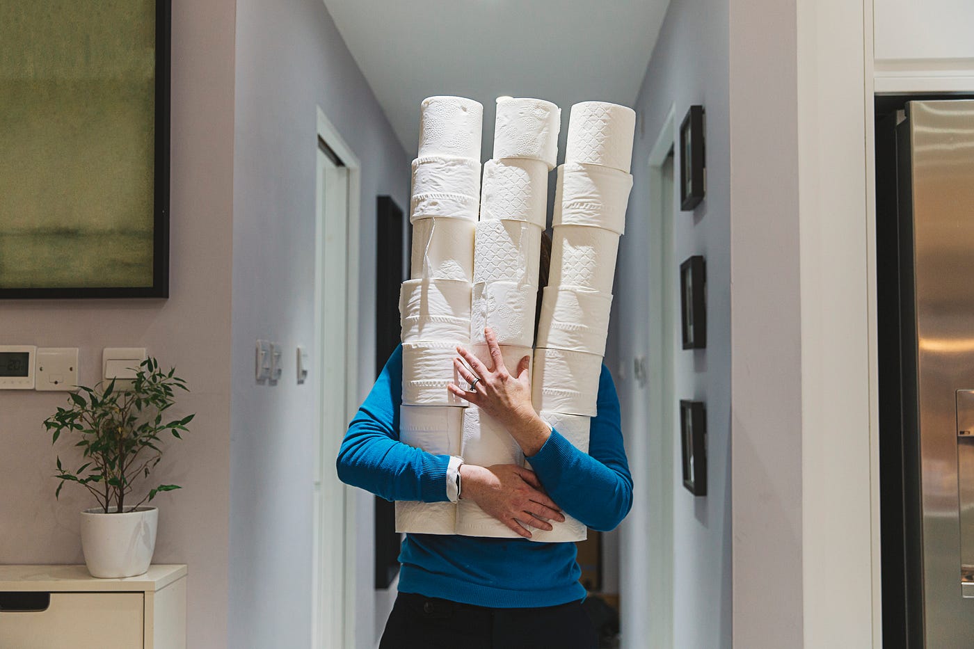 A photo of a person holding a tower of toilet paper rolls as they walk down the hallway.