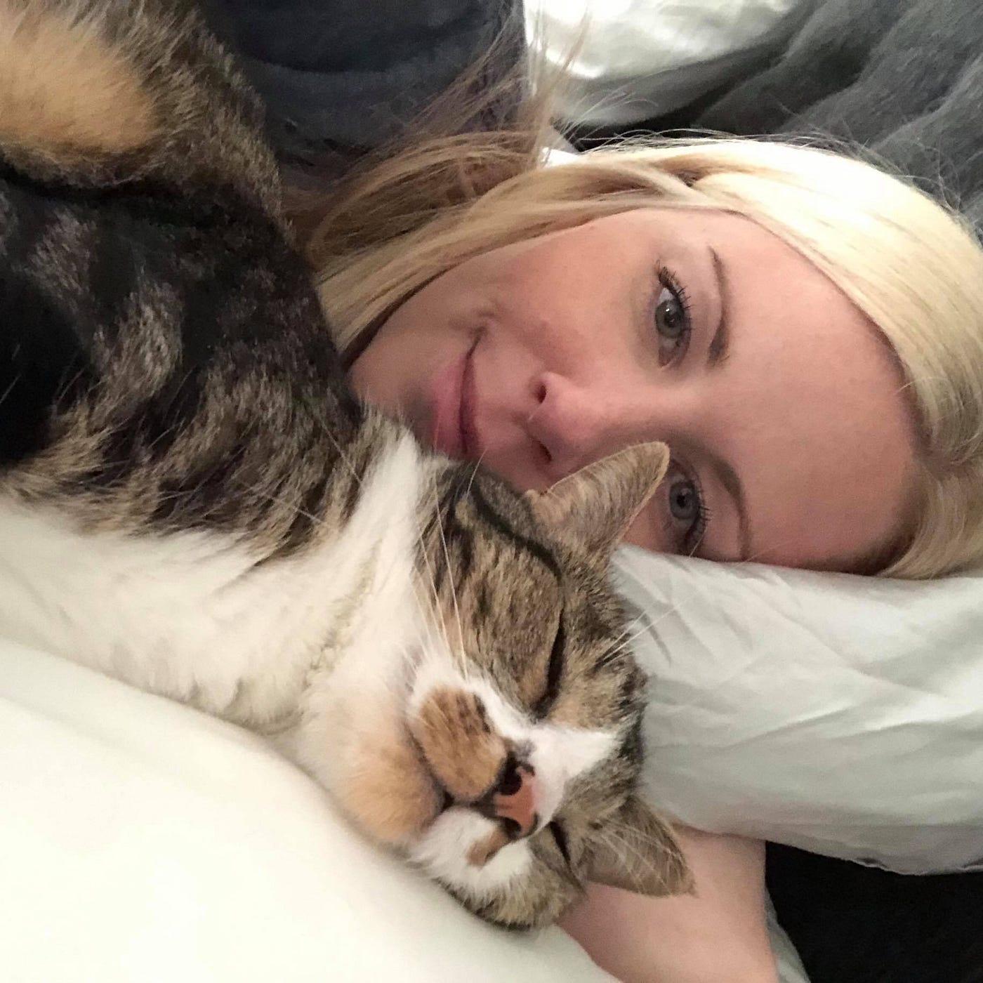 The author lying in bed with her cat sleeping in front of her.