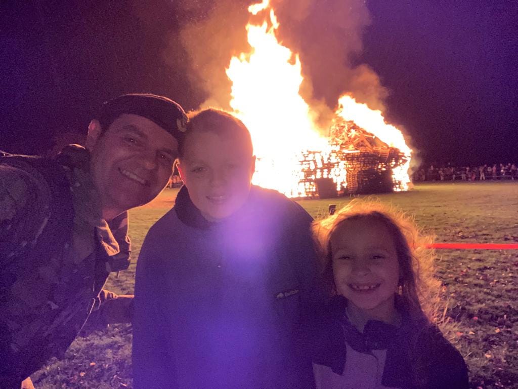 A man in RAF uniform smiles in front of a bonfire with his two children
