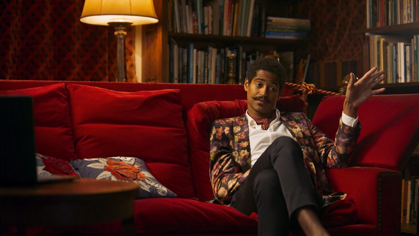 Dorian’s friend Henry sits for his interview on a lush red velvet sofa in a book lined room
