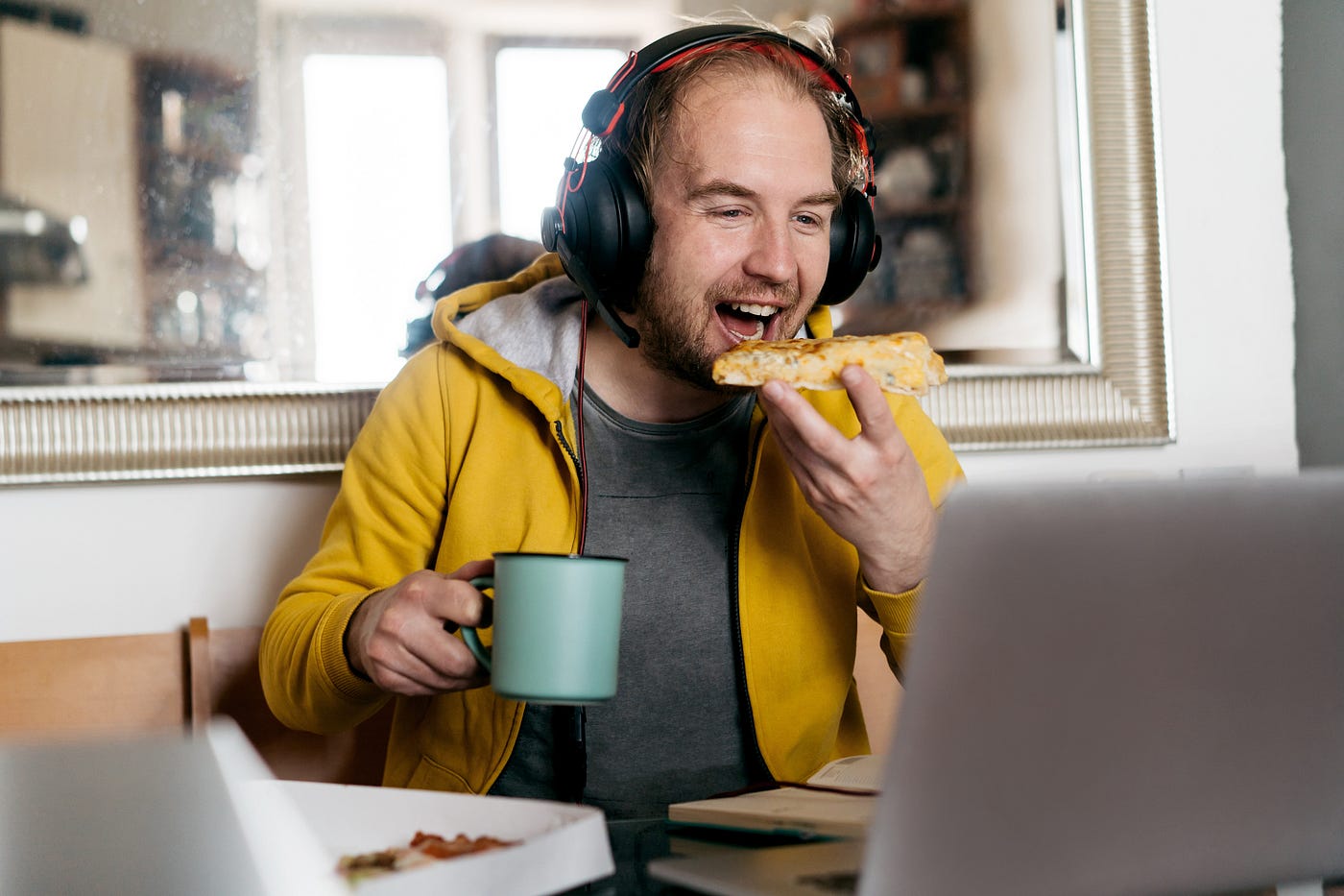 A photo of a man eating pizza and laughing while on a video call.