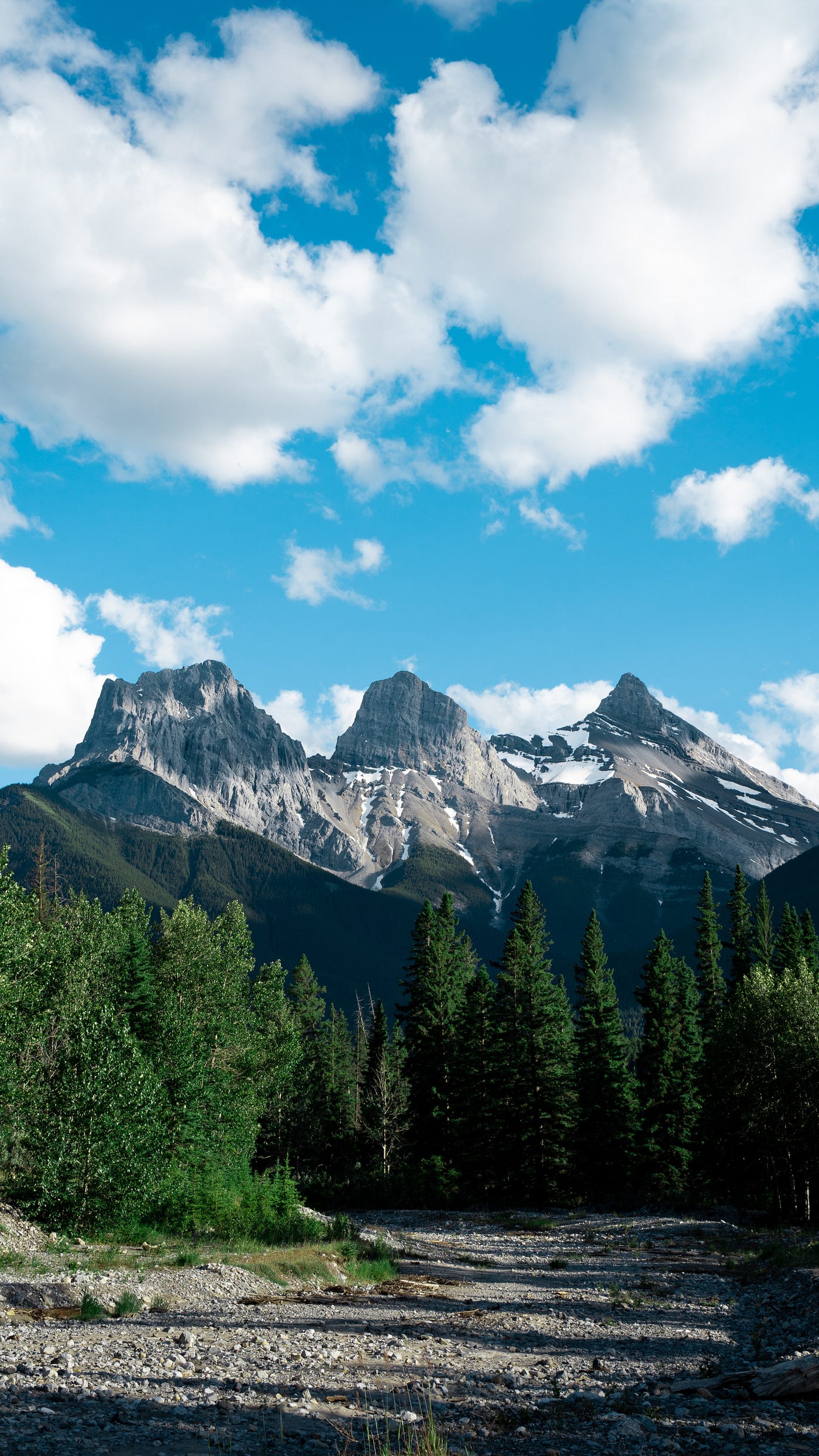The three sisters mountain peaks in Canada, with blue sky beyond and trees in the foreground