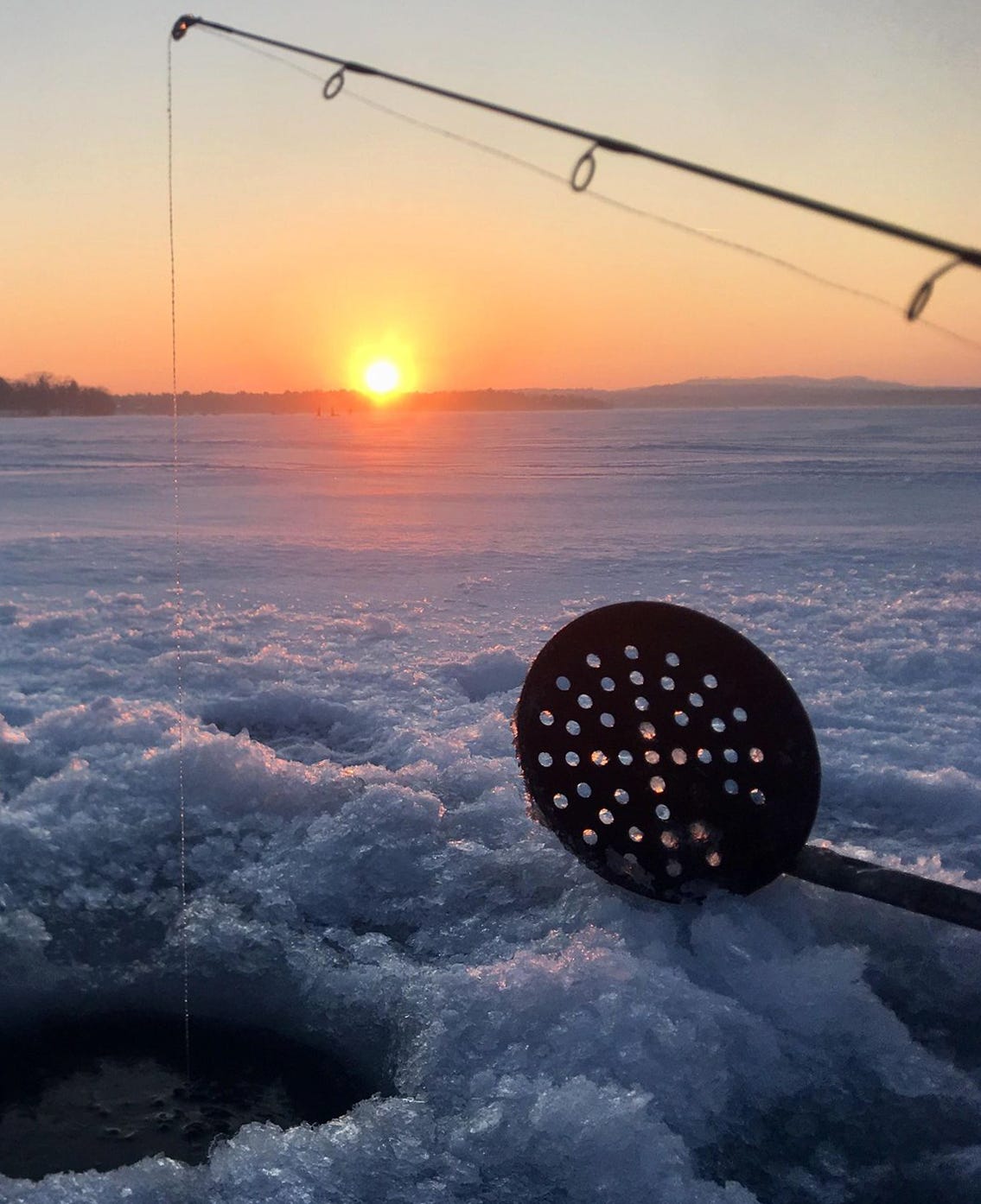 sunset on the ice with a close up of hole, scooper and fishing pole