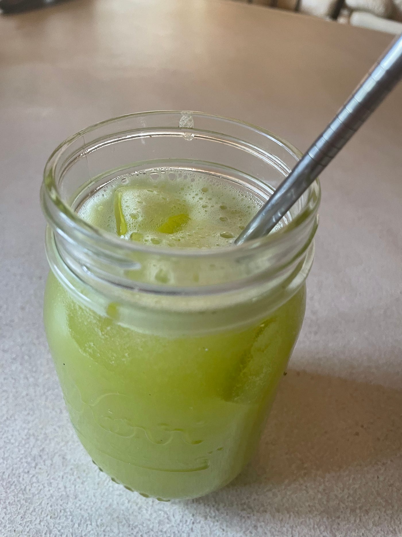 Celery juice in a glass jar with a straw on the counter.