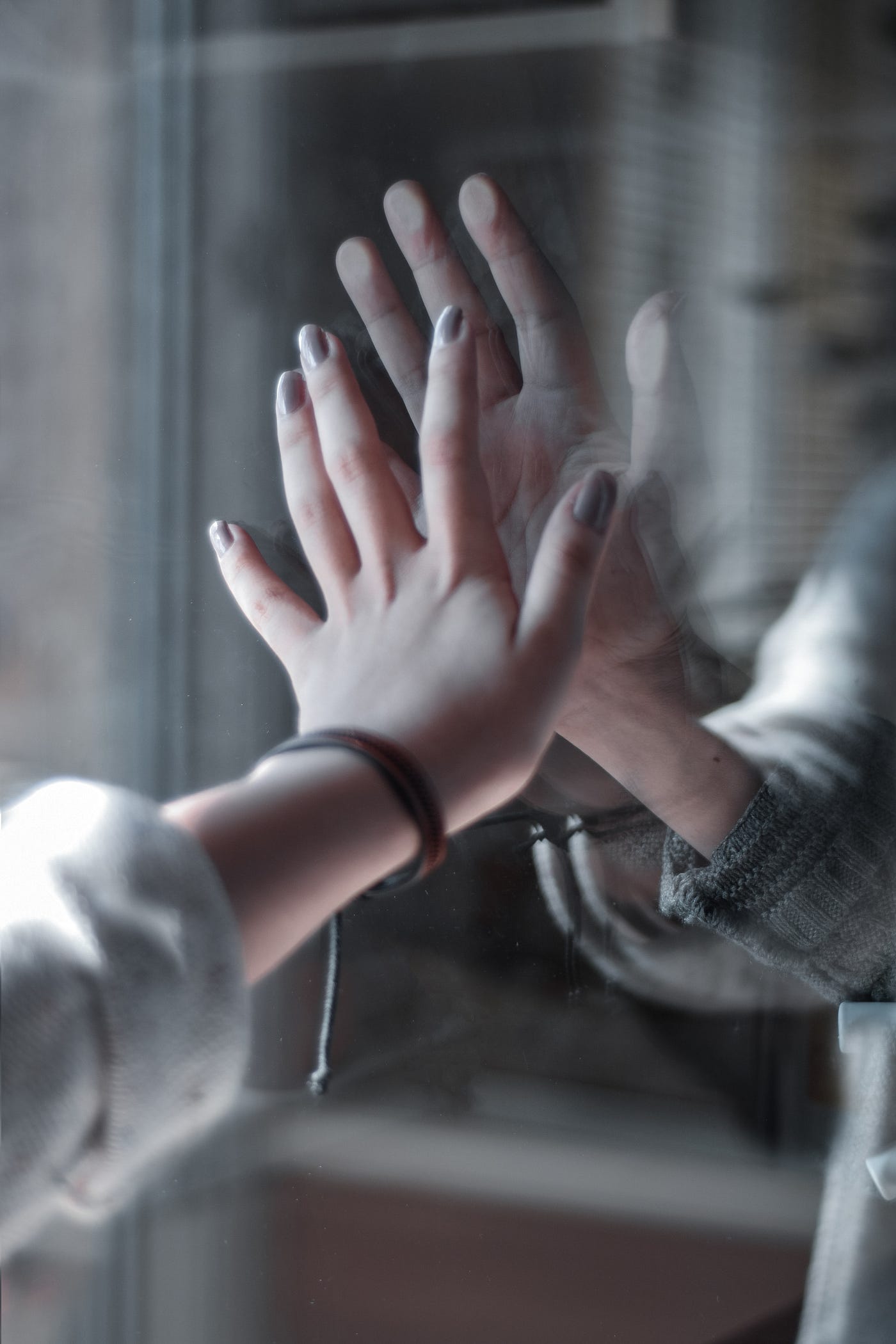 Mom and child are separated by glass and holding hands toward each other