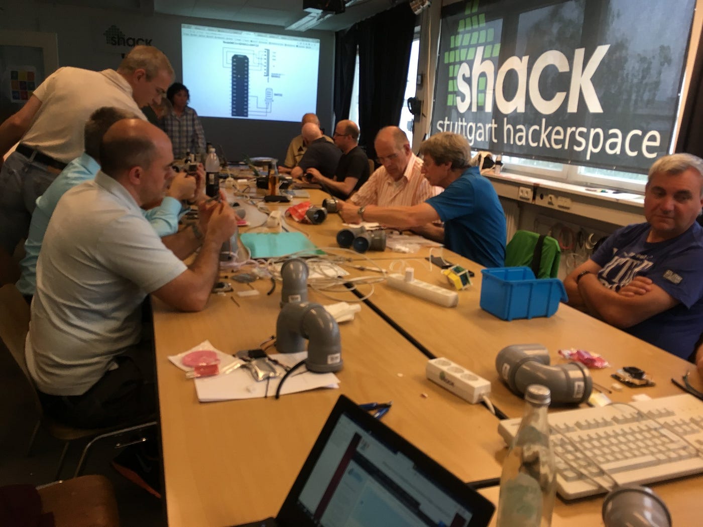 Several people sitting at a long conference table with a number of air quality sensors on the table.