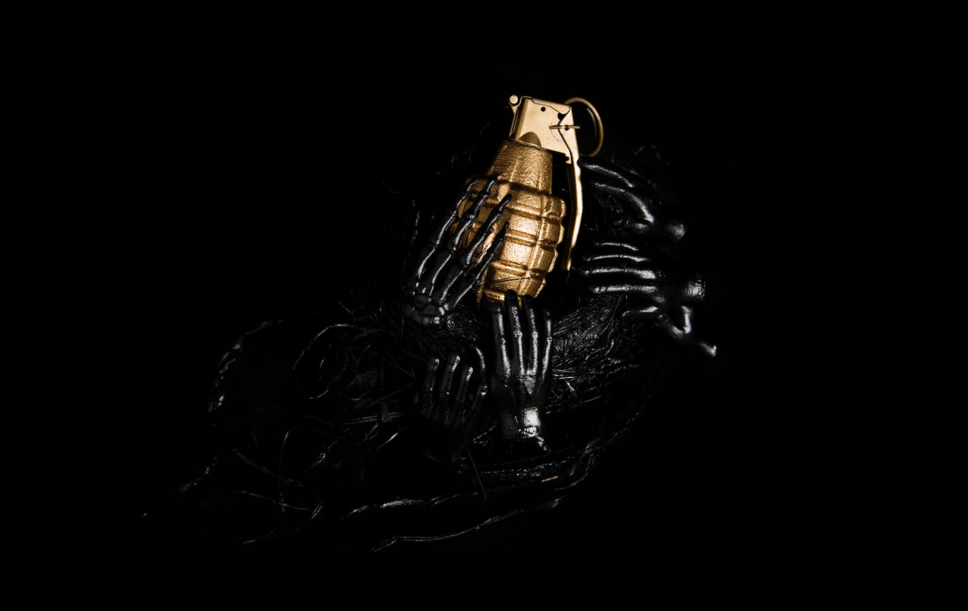 Several black, plastic hands grasping at a golden grenade.