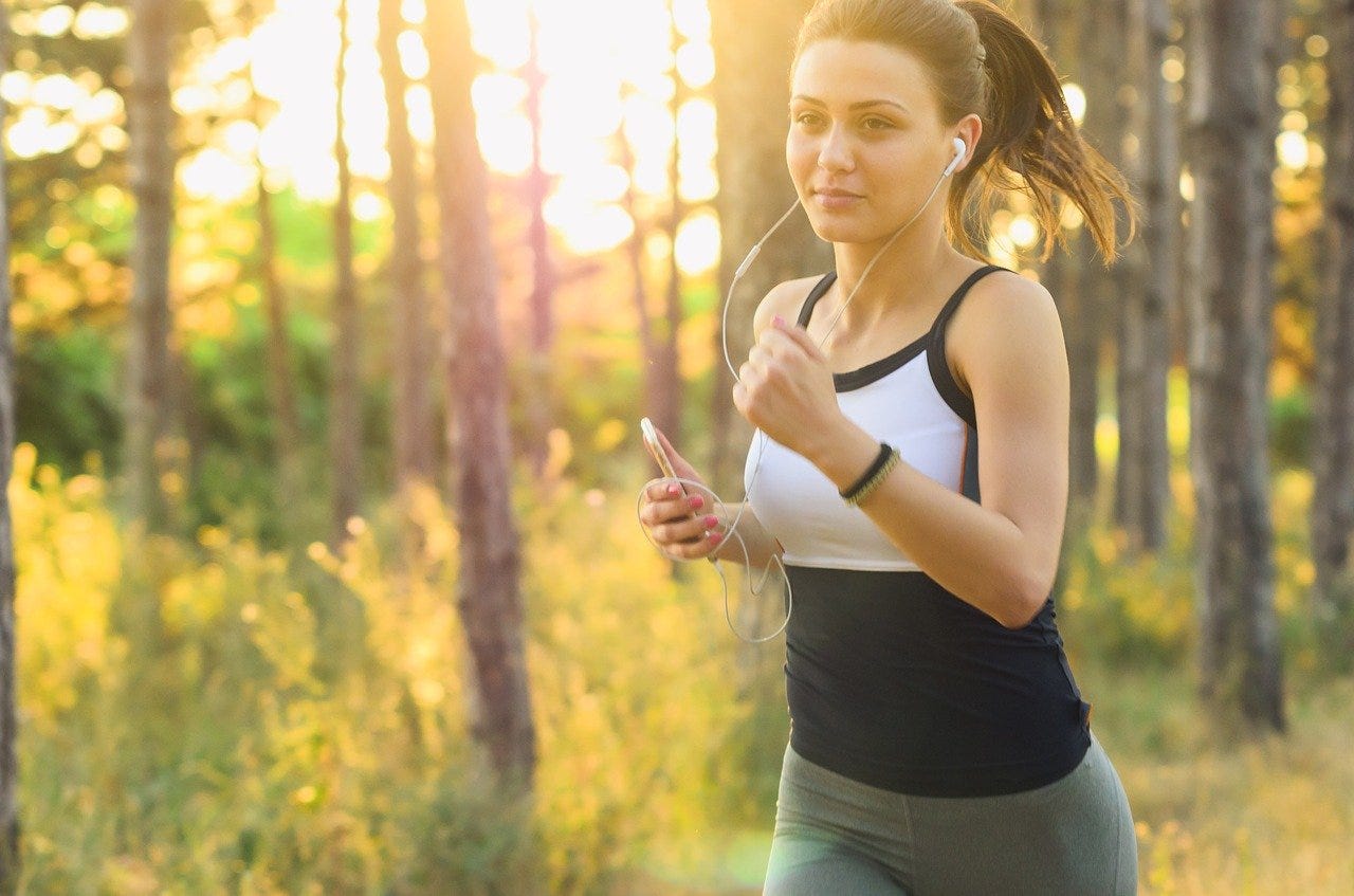 woman running through forest of trees at sunrise.