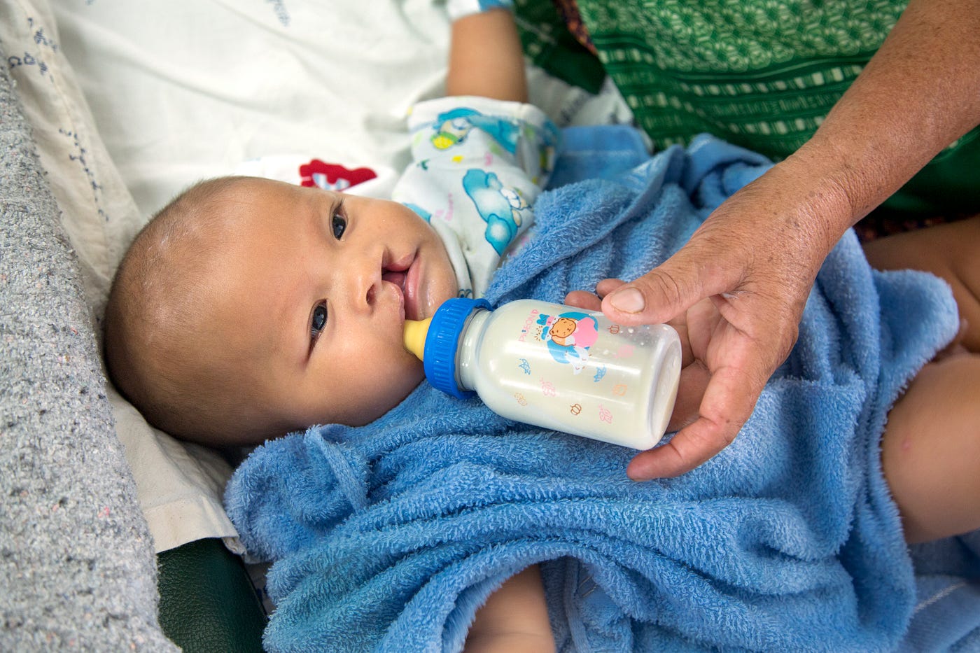 Pitchaya, a little boy from Thailand sucks on a bottle from his grandmother.