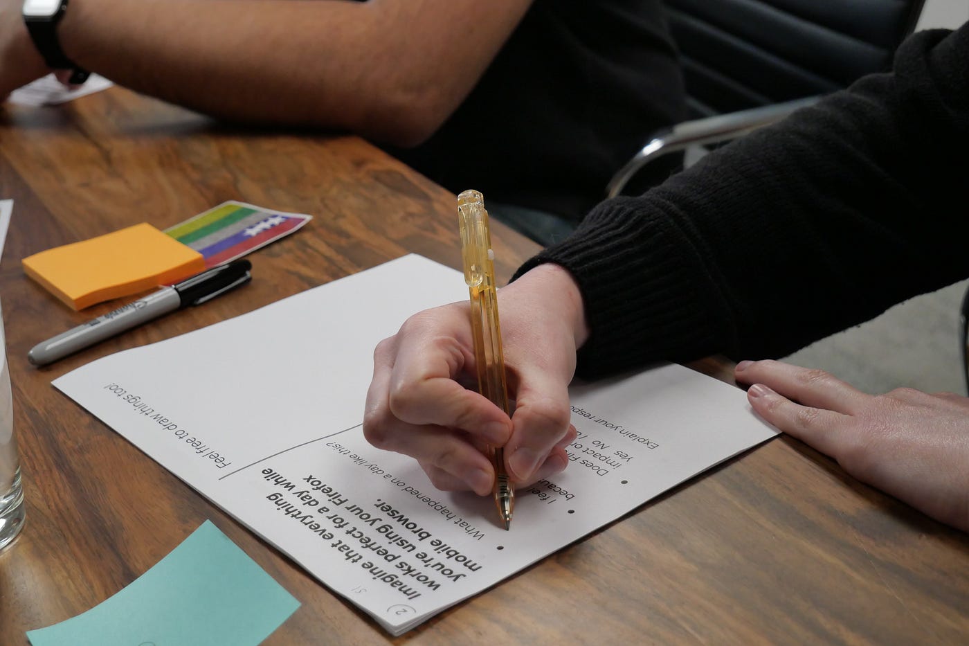 Image of a participant in a black long-sleeved shirt filling out a worksheet with an orange pen.
