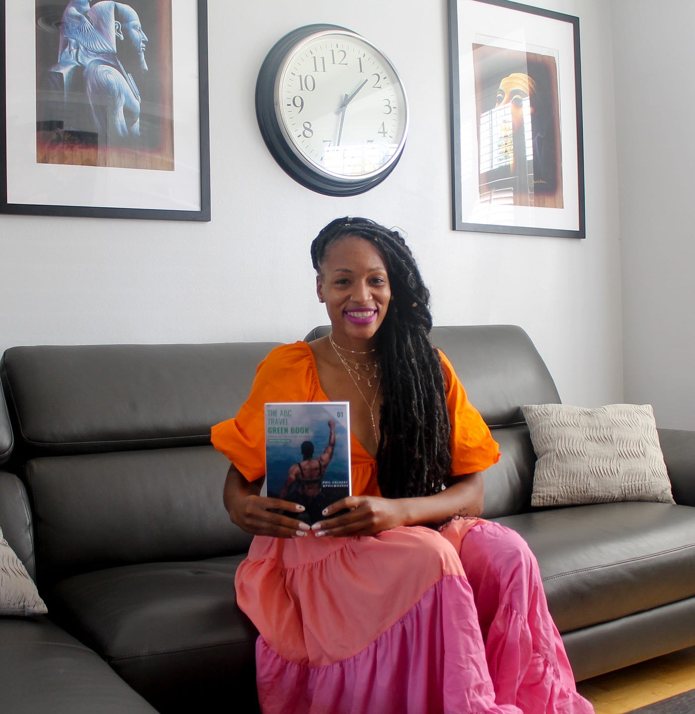 Martinique Lewis sitting on a black couch holding her book on her lap.