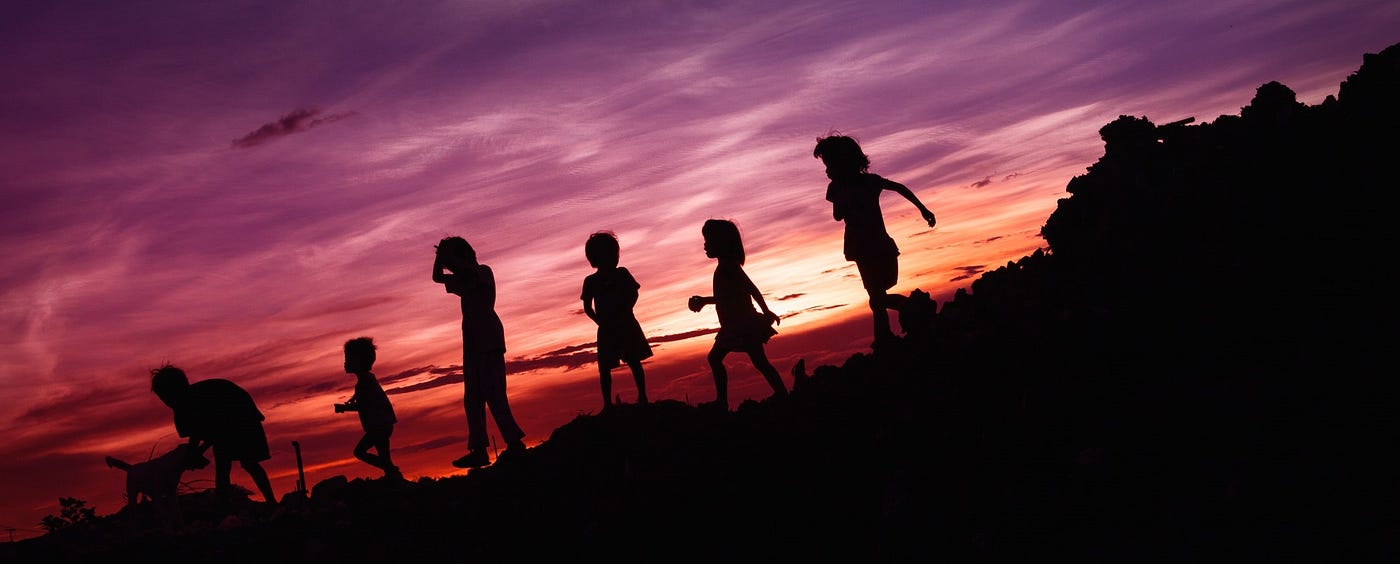 Silhouettes of several children playing outdoors in the evening.