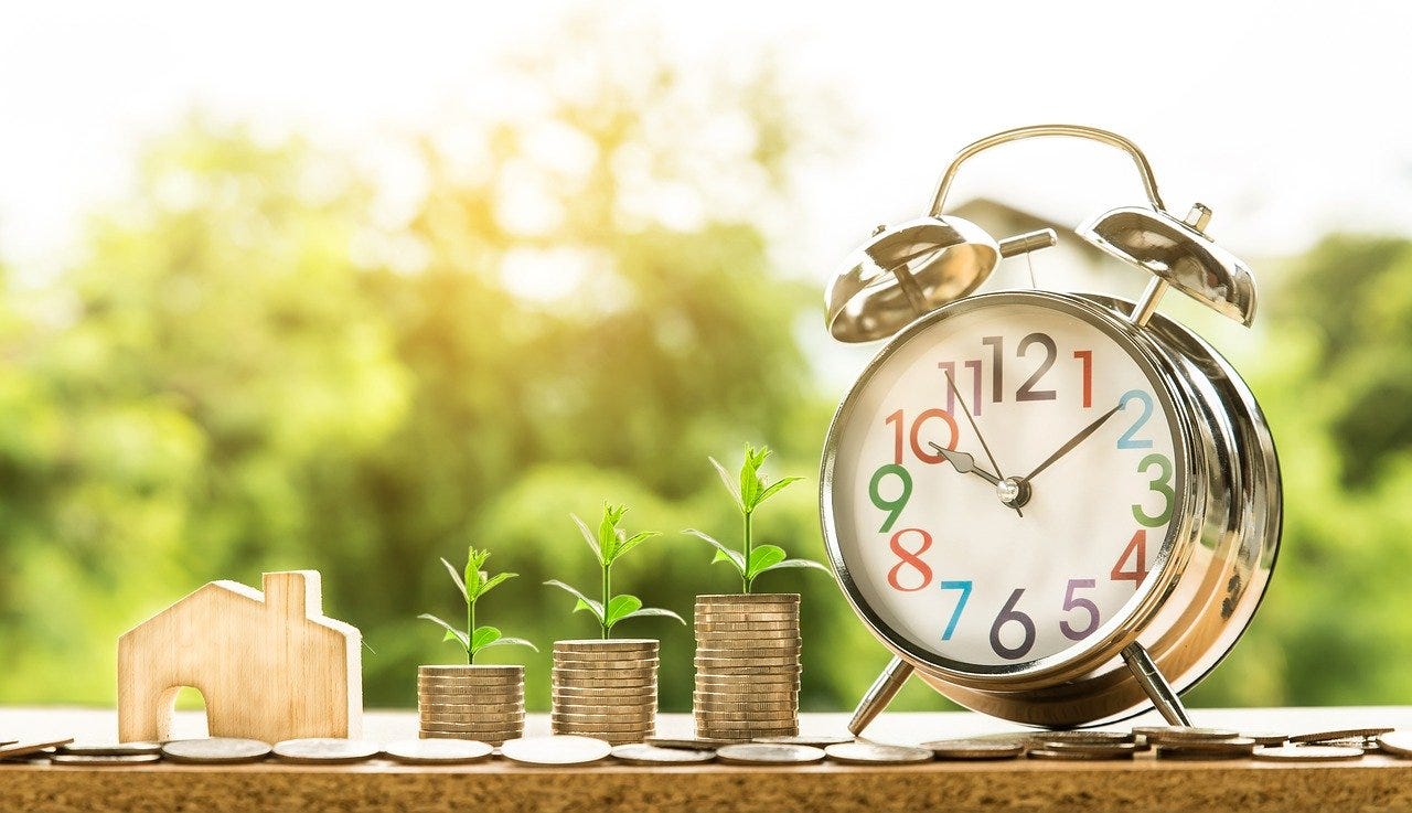 casa, moedas e relógio sobre mesa simbolizando tempo de investimento