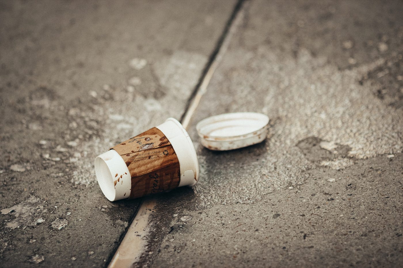A tipped over coffee cup with the lid popped off on a sidewalk