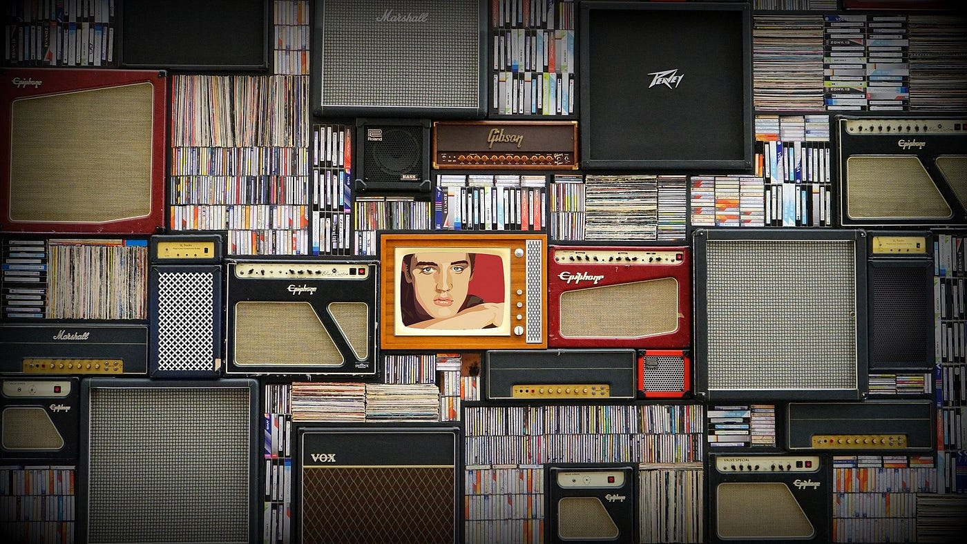 Old amplifiers, televisions and records. One of the televisions has an image of Elvis Presley on it.