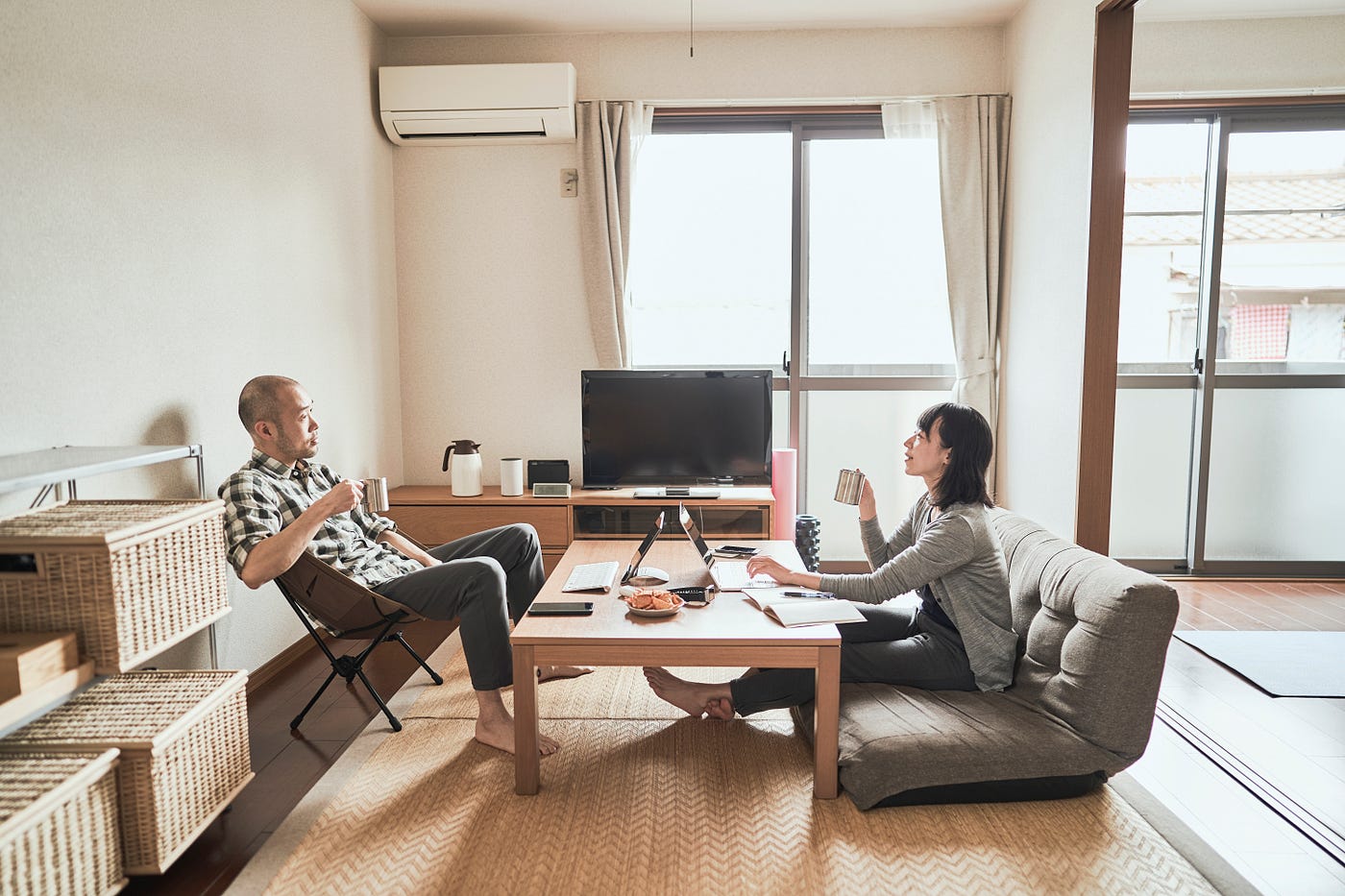 A couple sits on opposite sides of a coffee table, working on their laptops together at home.