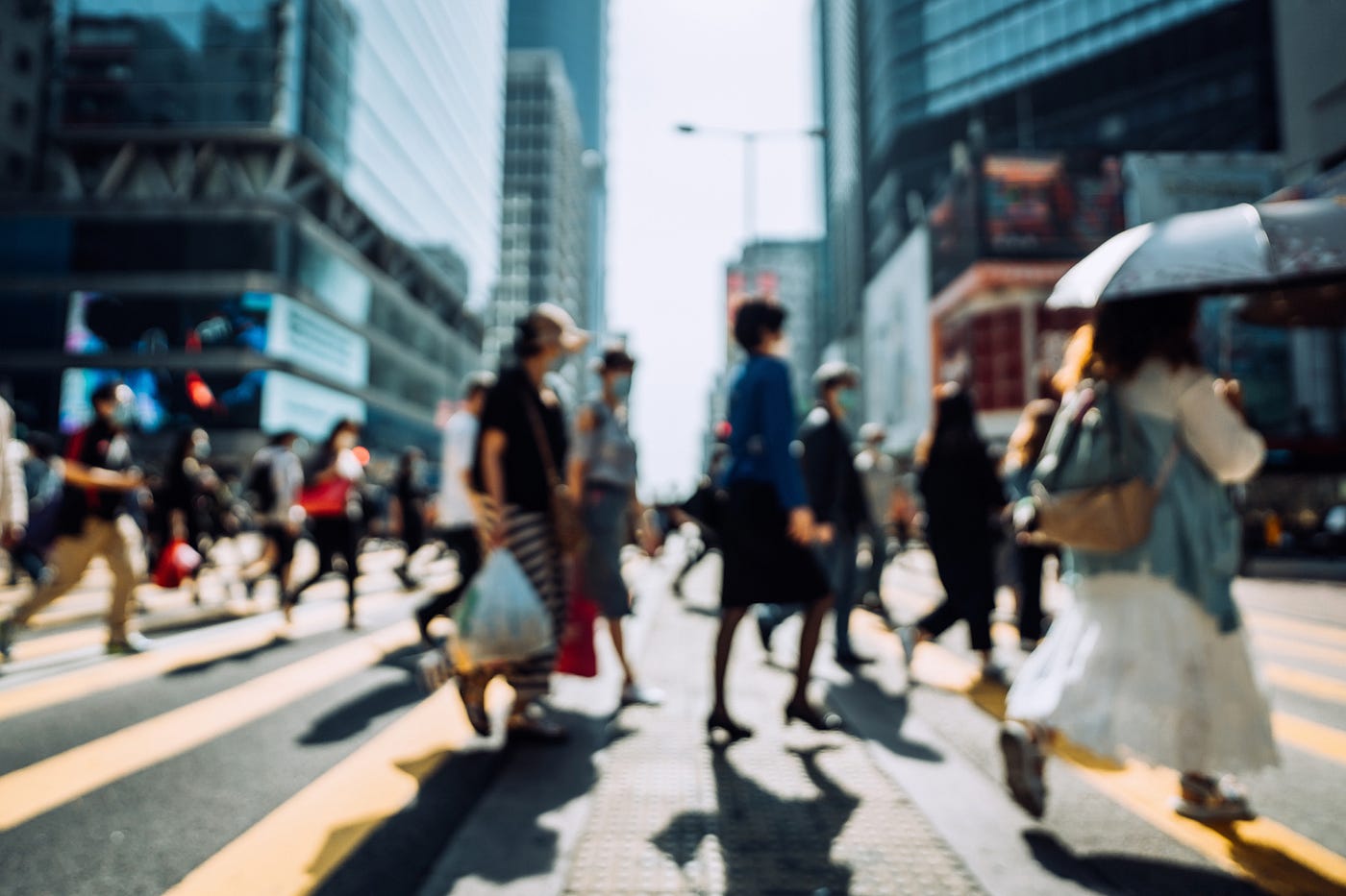 Blurred image of people walking at a crosswalk in a city.