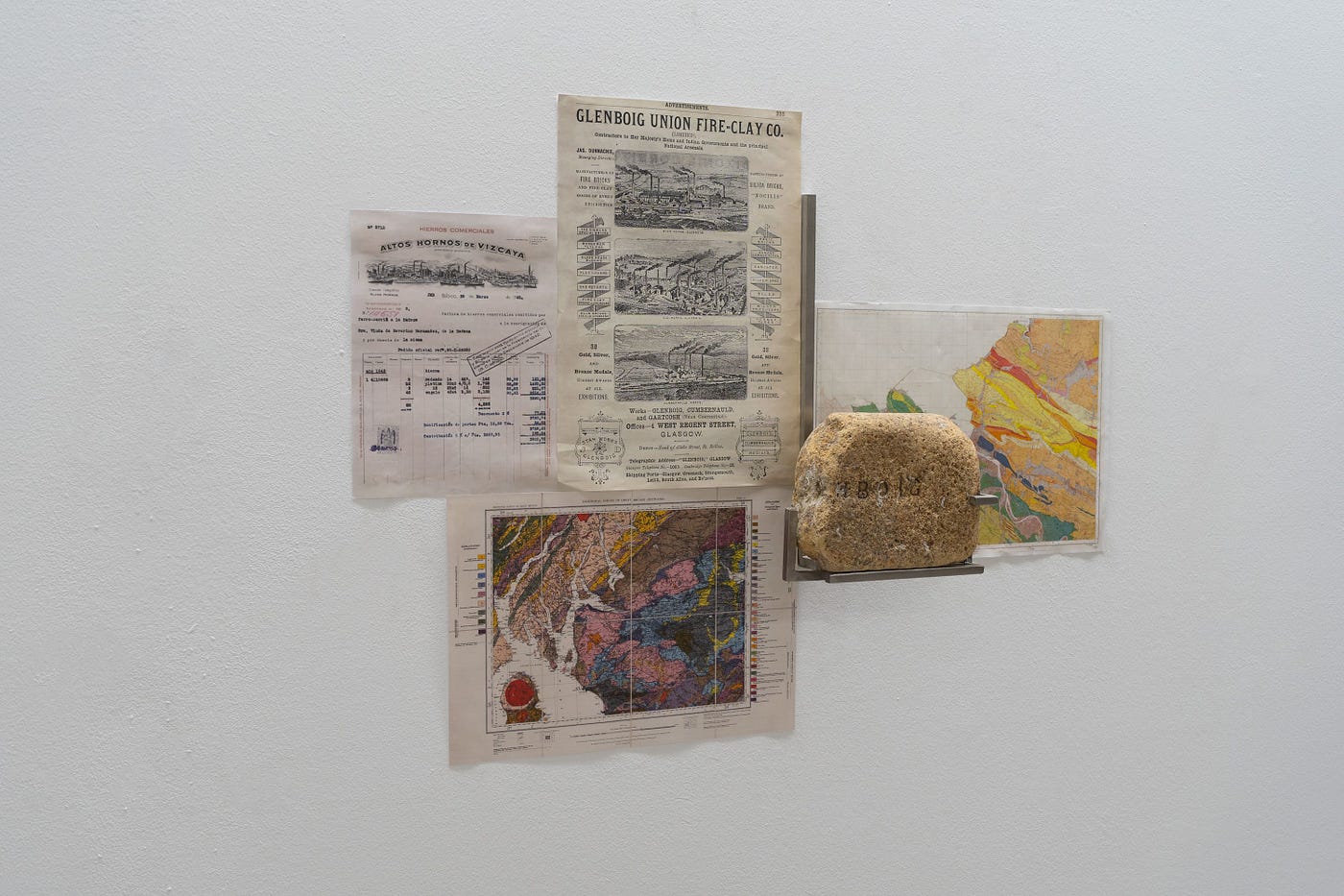 Four cuttings from magazines, a map and a rock hanging on a wall.