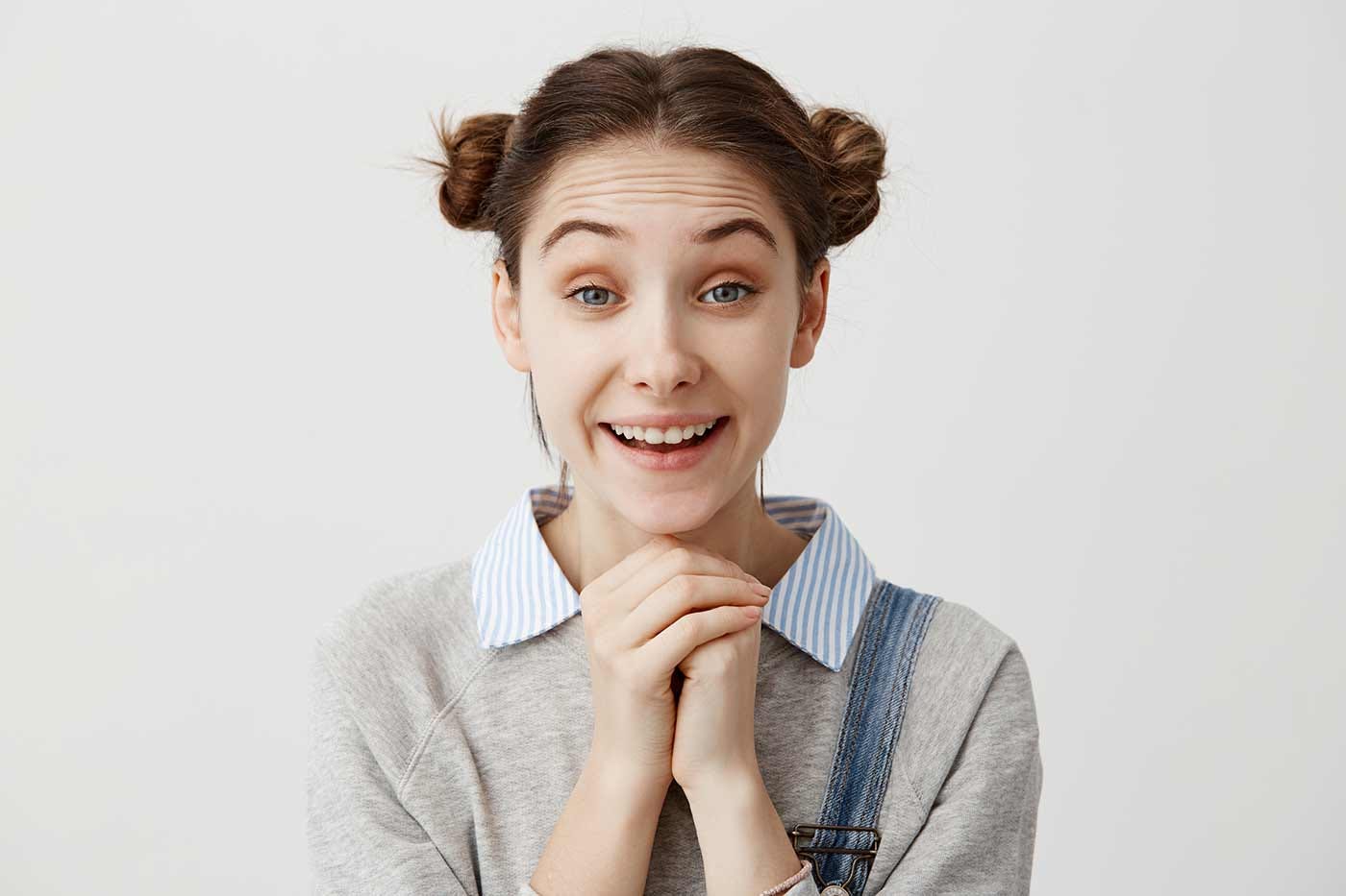 Young woman with hands folded beneath her chin smiling, as if anticipating good things.