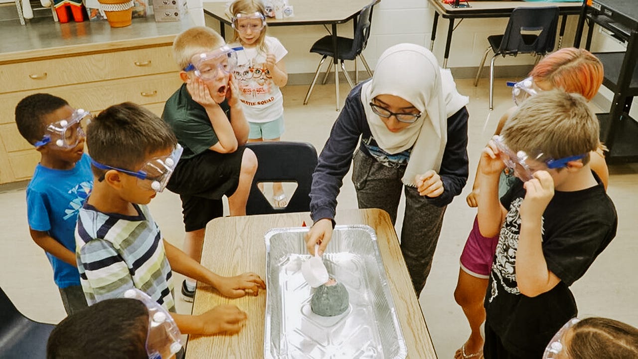 Nora pours a solution into a volcano-like science experiment with children
