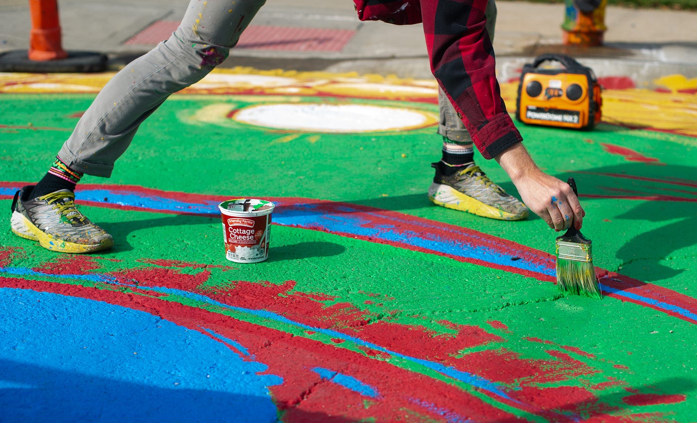 A close-up of an artist wearing sneakers painting the details of a colorful patch of asphalt.