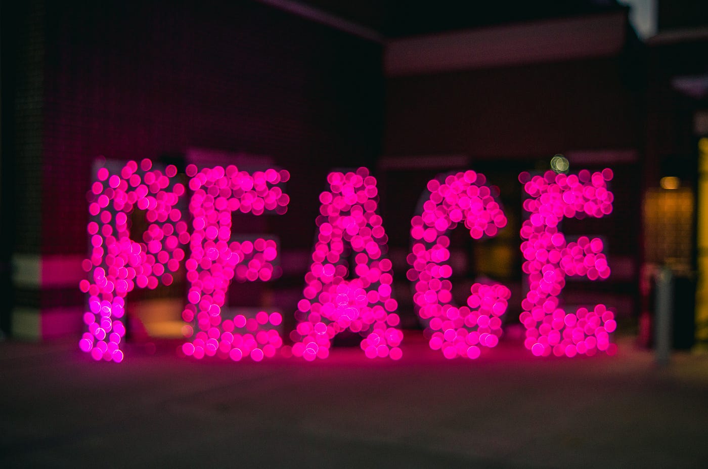 Bright pink lights spell out the word “Peace” on a black background.
