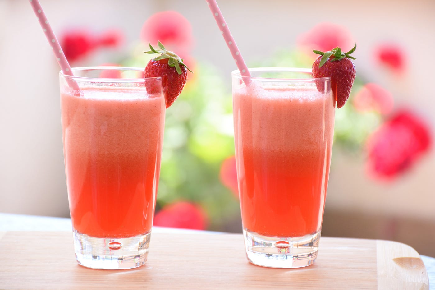 Two glasses on a counter filled with strawberry juice with a freash strawberry on the side of the glass and a cute pink straw.