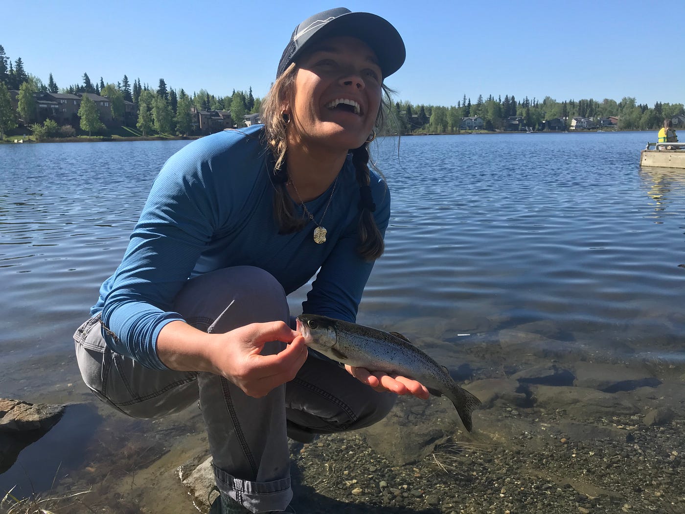 young woman holding a fish by a lake