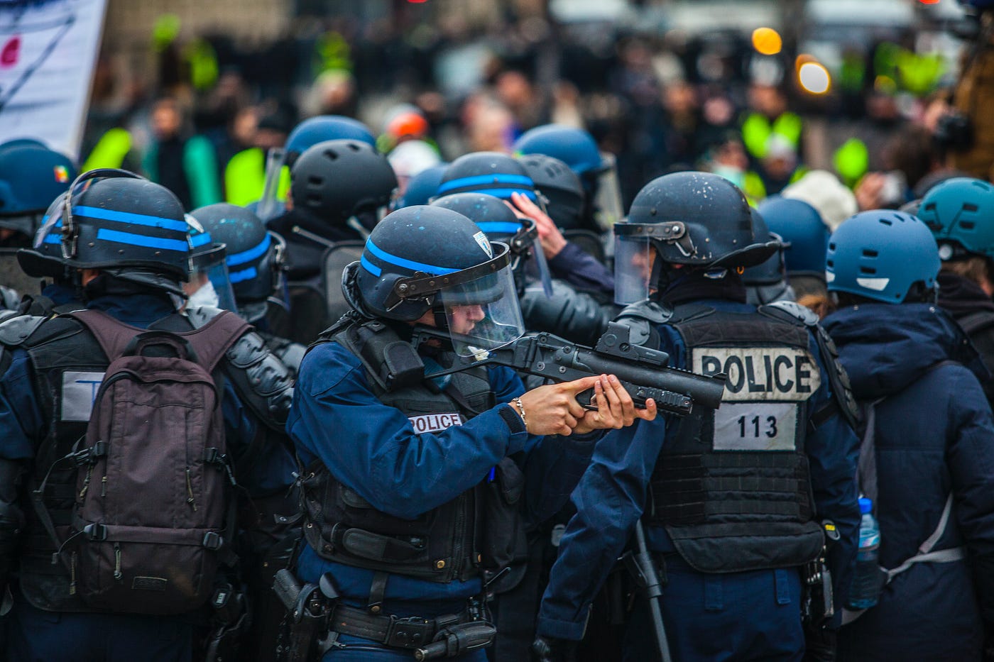 police in riot gear aiming a gun