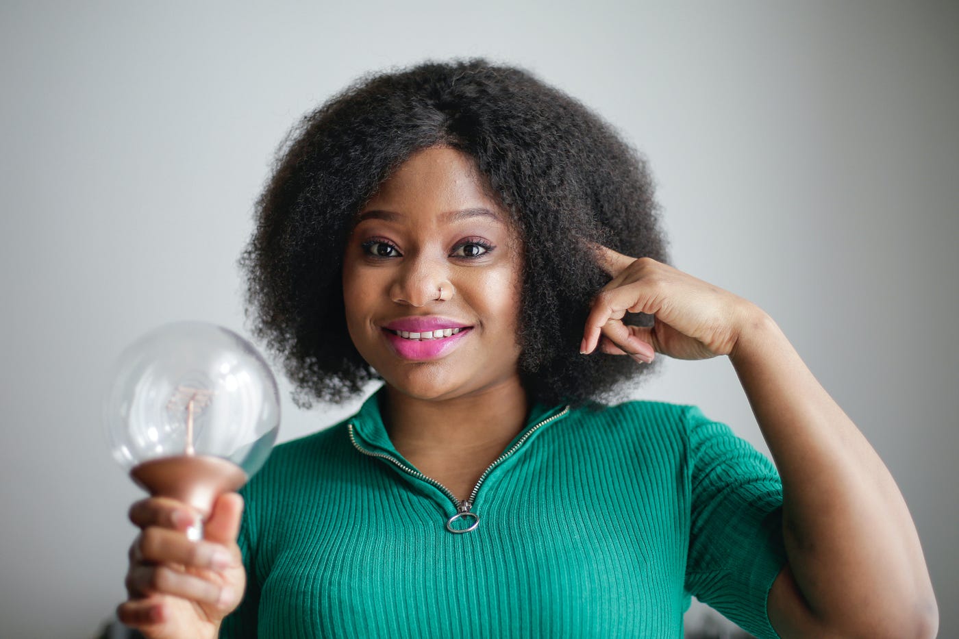 A curious looking woman holding a light bulb and pointing to her head