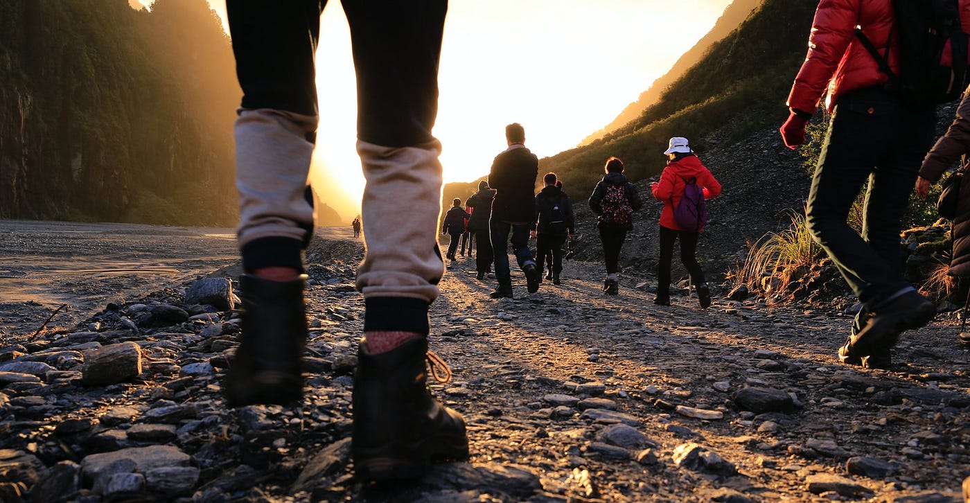 Group of people walking along a rocky path toward sunlight.