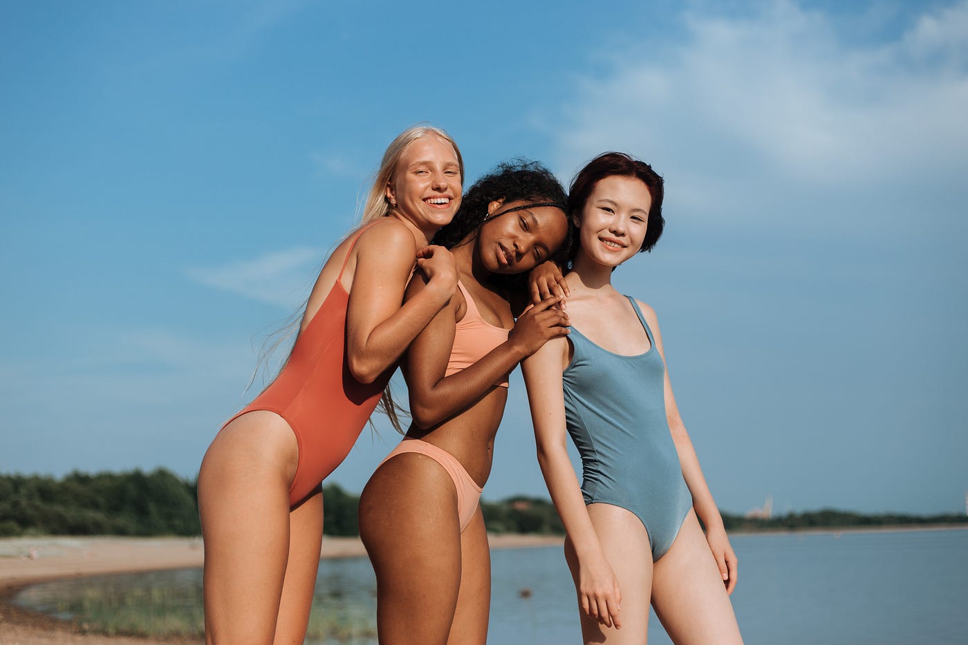 Three girls are standing next to each other on a beach.