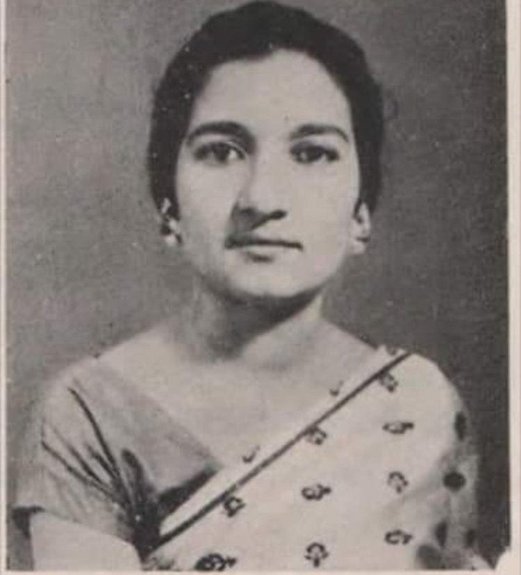 A grainy, old photo of a young woman looking directly into the camera with a grey background.