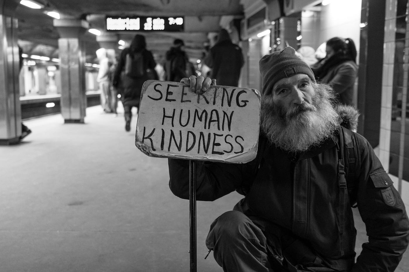 Homeless man holding up a sign that says “Seeking human kindness”