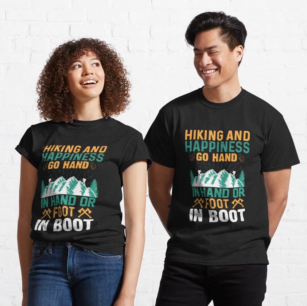 Man and Woman Wearing a black classic t-shirt with amazing illustration and text saying “hiking and happiness go hand in hand or foot in boot”.