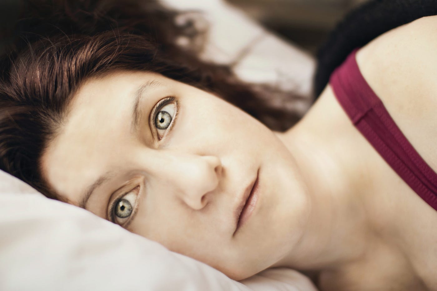 A wide-eyed woman rests her head on a pillow, suffering from insomnia.
