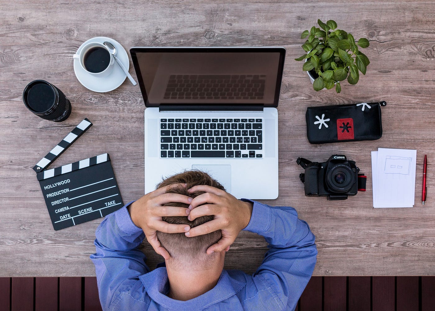 Writer bows over a laptop with hands clasped at the back of their head