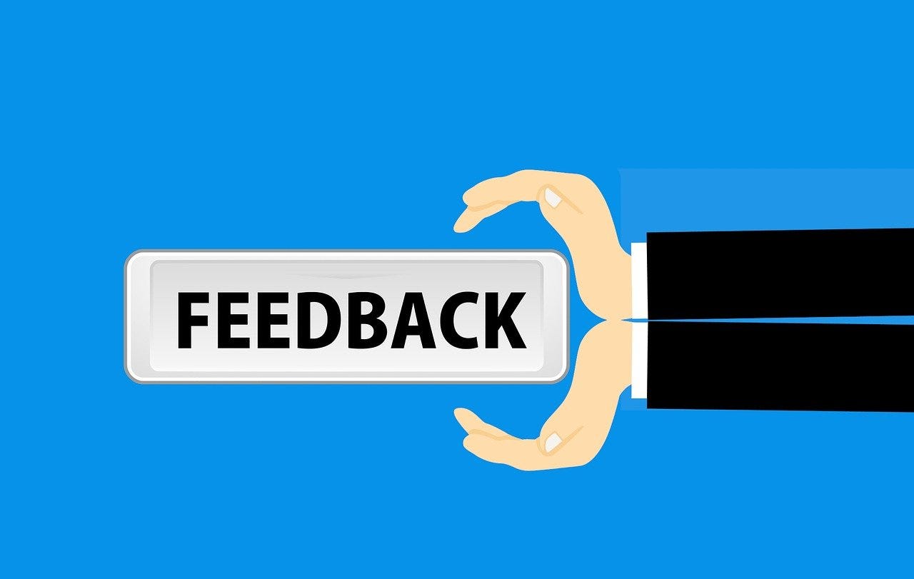 IMAGE: On a blue background, a drawing of two hands holding a sign that says “FEEDBACK” in capital letters