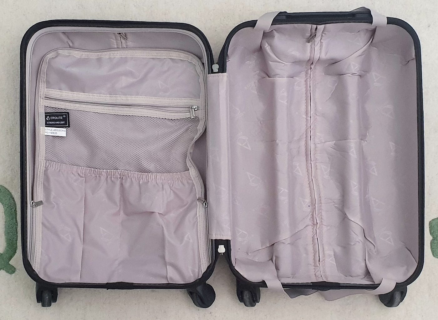 An image of an empty open suitcase on a rug. The suitcase lining is light grey. The dark grey exterior of the suitcase is just visible.