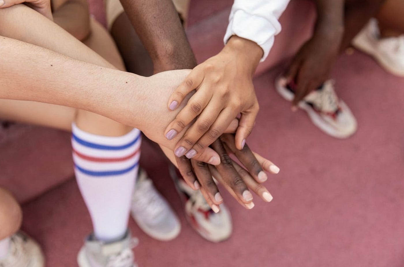 A view of dark and light skinned hands piled atop one another as a symbol of being united with the peoples’ shoes in view underneath.