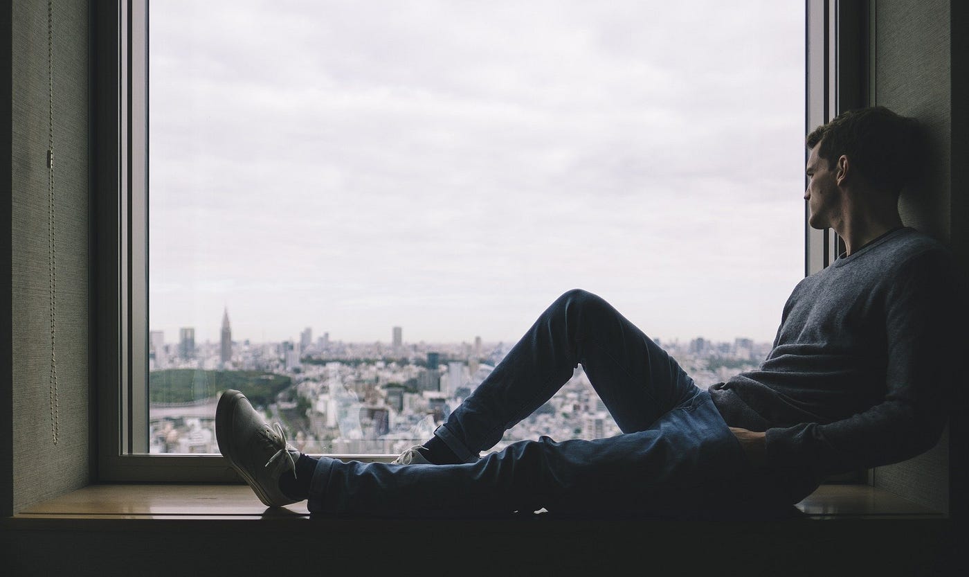 A man sitting alone in a window sill overlooking a city.