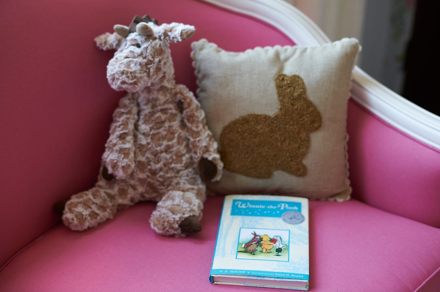 Details of an oversized reading chair in white and fuchsia pink, with an embroidered pillow, stuffed animal, and a children’s book.