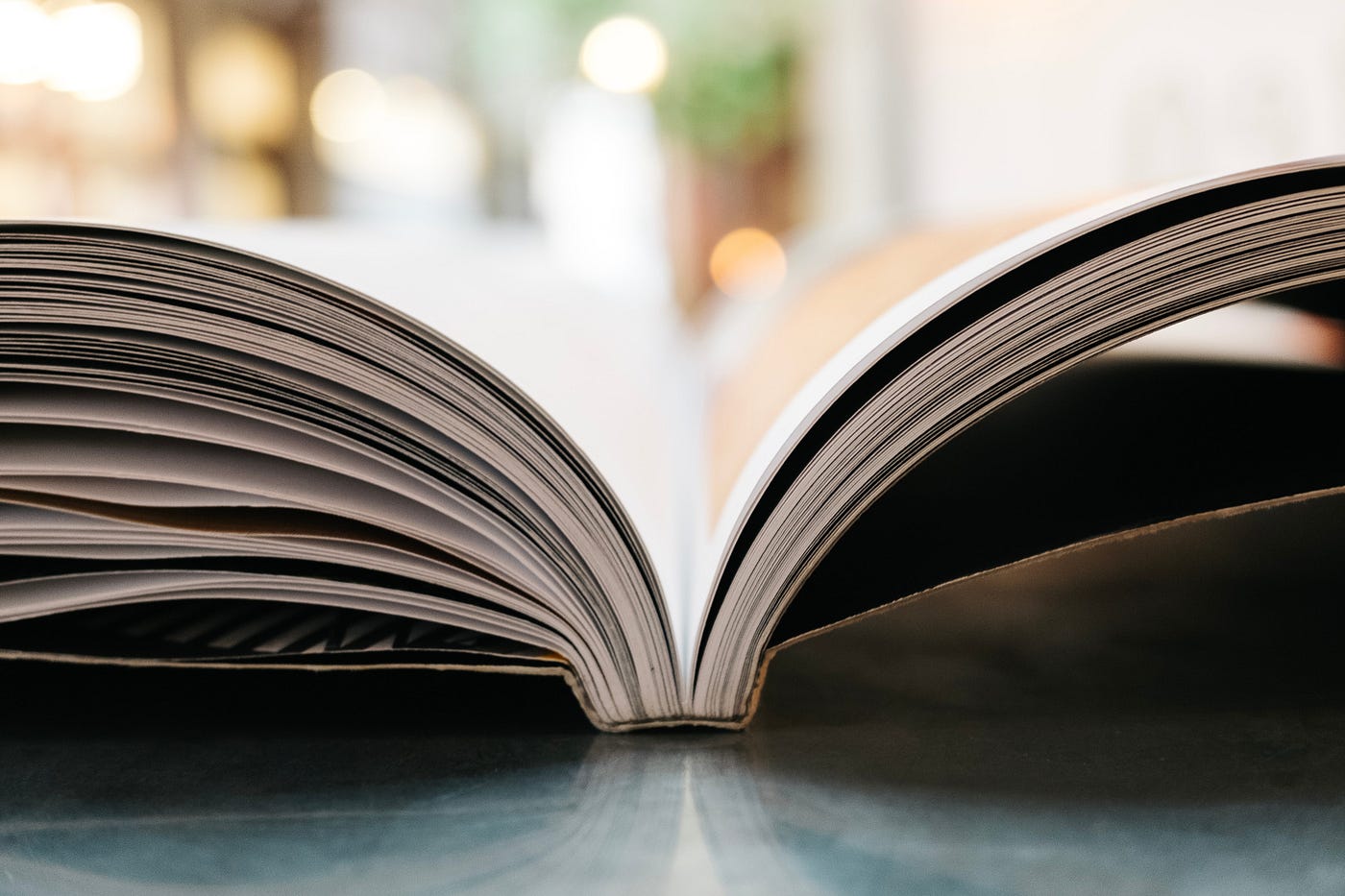 A book with its pages splayed sits on a table. There are blurred lights in the background.