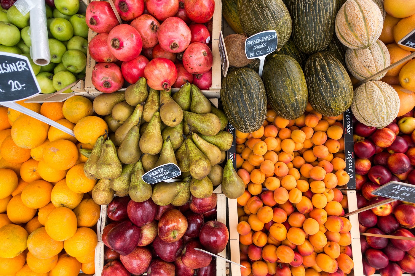 Picture of various fruits in bins at a market: apples, oranges, pomegranates, etc.