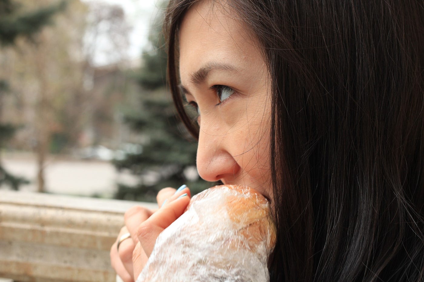 A white woman with dark hair eating a sandwich outdoors